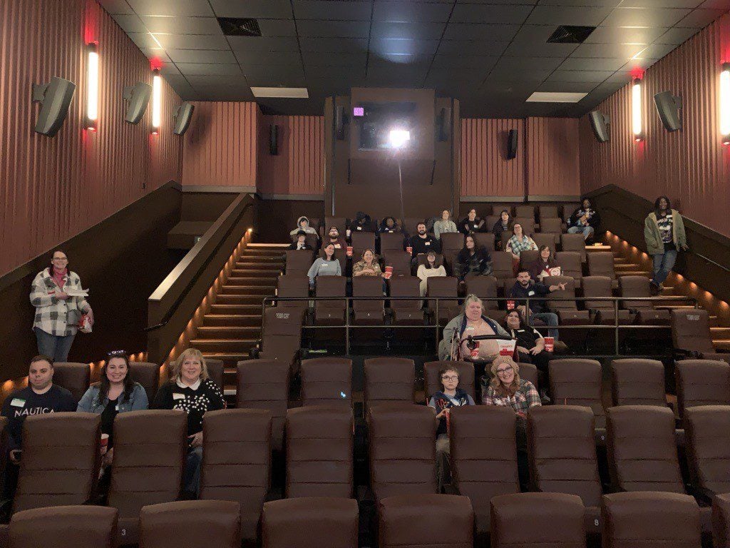 Adults and children sit in a movie theater with snacks and drinks.