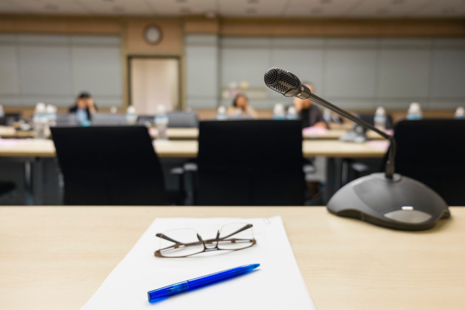 view of a meeting room from behind a desk with a microphone, pen, and glasses sitting on it